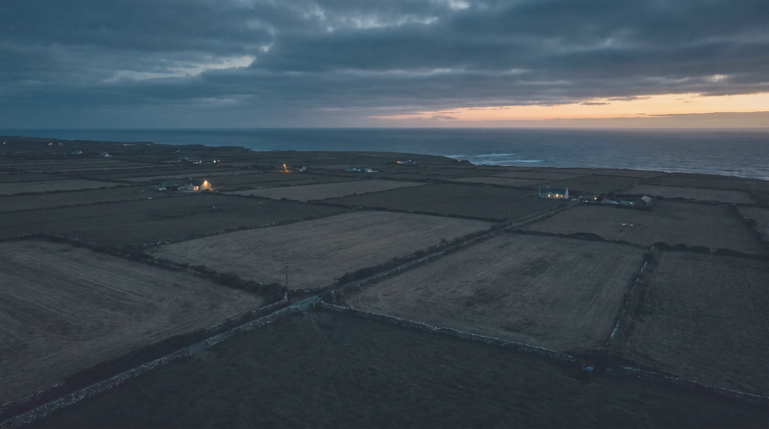 Aerial view of Irish coastal farmland at dusk with lit farmhouses